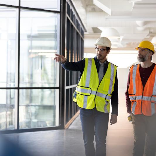 2 workers in safety gear walking down a hall