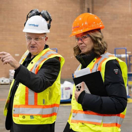Professionals in safety gear discussing a key part of Essentials of Sales and manufacturing jobs at a Saint-Gobain production facility.