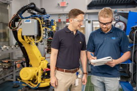 Two engineers at Saint-Gobain North America are discussing notes beside industrial robotic equipment, representing careers in the manufacturing industry.
