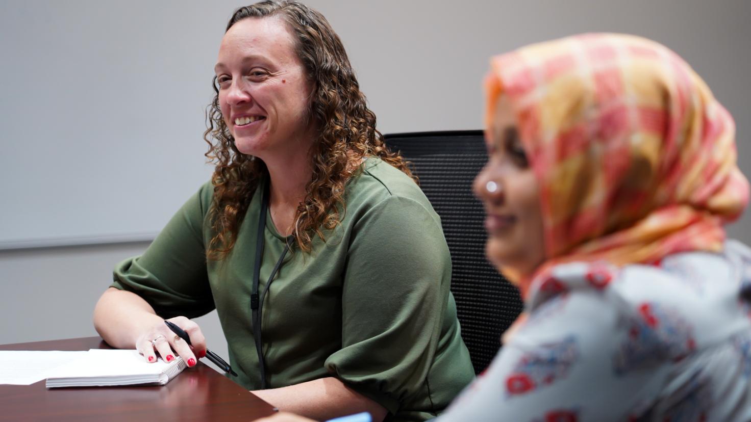 Two women seated at the corner of a conference table.