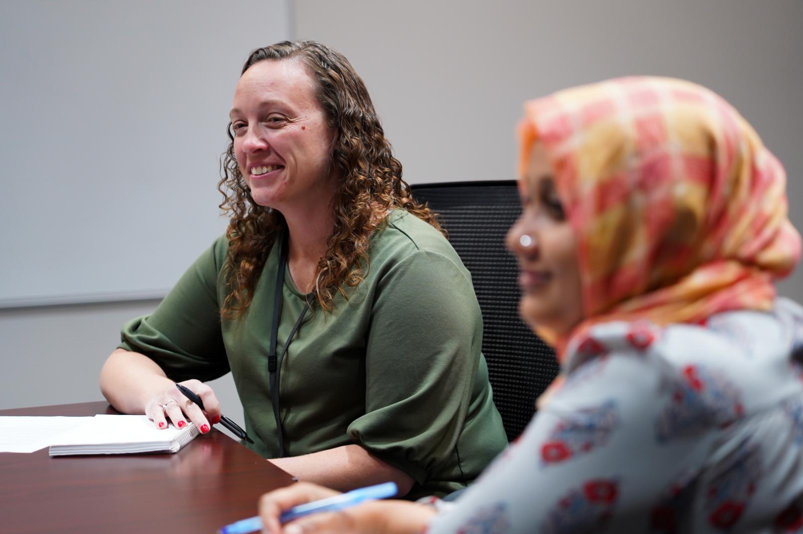 Two women seated at the corner of a conference table.